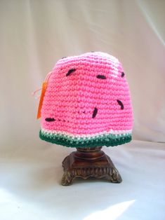 a crocheted watermelon hat sitting on top of a wooden stand with a white background