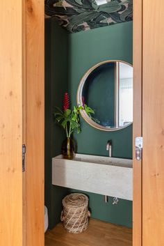 a bathroom with green walls and wood trimmings on the ceiling, along with a round mirror