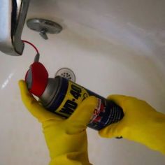 a person in yellow rubber gloves is cleaning a sink with a spray bottle and sponge