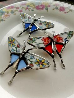 three butterfly shaped brooches sitting on top of a white plate with floral designs