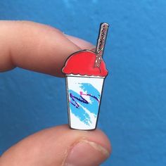 a hand holding a small pin with a drink on it