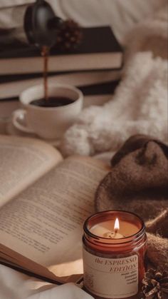 an open book with a candle on top of it next to a cup of coffee