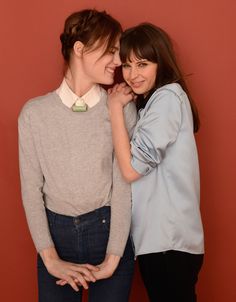 two young women standing next to each other in front of a red wall and smiling