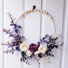 a wreath with white and purple flowers hanging on a wooden door frame in the shape of a circle