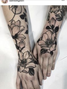 two hands with black and white flowers tattooed on them, one holding the other's hand