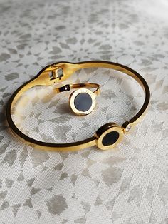 Luxury golden bracelet and ring set with hinge and ends in the shape of a black stone, golden color, women's gift, wedding gift, A golden zinc alloy bracelet and its fashionable ring in the shape of a black stone too, with a chic personality , European and American style, high-end atmosphere, exaggerated simplified geometric abstract patterns, vintage, chic, luxurious, elegant, suitable for daily travel, friends gathering, romantic vacation, women's fashion show, business meetings business and all kinds of occasions. This rigid gold-plated bracelet, open, its luxury silhouette which wraps naturally around your wrist. With its shape and trend, it will attract all eyes. Bracelet And Ring Set, Golden Bracelet, Bracelet And Ring, Friends Gathering, Romantic Vacations, Gold Plated Bracelets, Geometric Abstract, Golden Color, Black Stone