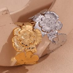 Add a touch of playfulness to your outfit with our Flower Cluster Cuff! This statement cuff bracelet features a cluster of beautiful flowers, bringing a whimsical and unique element to any look. Perfect for those who don't take themselves too seriously and like to add a bit of fun to their style. DETAILS & SIZE Finish: 18K gold plate Material: Stainless Steel Measurements: Diameter: 2.2"; Width: 1.5" Weight: 35 grams Waterproof, tarnish-resistant, and nickel free Shop Bracelets to curate your arm stack! Adjustable Flower Ring For Party, Spring Wedding Metal Bracelets, Adjustable Flower Cuff Bracelet For Spring, Spring Flower Metal Bracelets, Spring Flower-shaped Metal Bracelets, Arm Stack, Ear Bar, Statement Cuff Bracelet, Flower Cluster