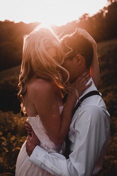 a man and woman are kissing in the field at sunset, with the sun shining behind them