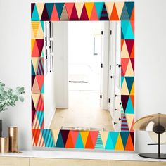 a brightly colored mirror sitting on top of a wooden dresser next to a potted plant