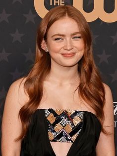 a woman with long red hair wearing a black dress and diamond earrings smiles at the camera