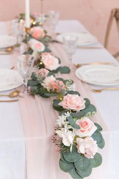 the table is set with white and pink flowers, greenery and candlesticks