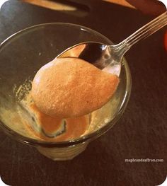 a spoon with some food in it on top of a glass bowl next to an orange