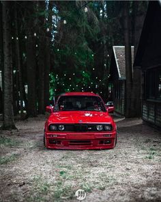 a red car parked in the middle of a wooded area with lights strung up behind it