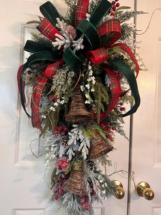 a christmas wreath hanging on the front door with bells and evergreens attached to it