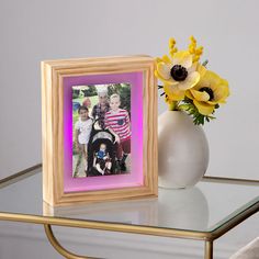 a vase filled with yellow flowers next to a photo frame on a glass top table