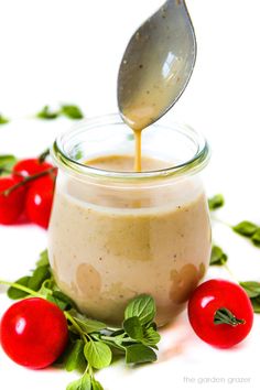 a spoon pouring dressing into a jar with cherry tomatoes on the table next to it