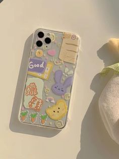 an iphone case with stickers on it sitting next to a stuffed animal and cloth