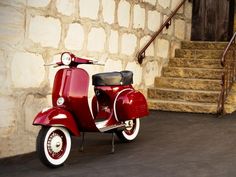 a red scooter parked in front of a stone building with steps leading up to it