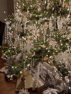 a christmas tree is decorated with silver and white ornaments, wrapped presents under the tree