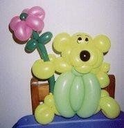 a balloon bear holding a flower on top of a blue table with balloons in the shape of flowers