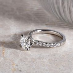 a white gold engagement ring with diamonds on the side and a feather in the background