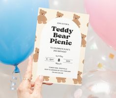 a person holding up a teddy bear picnic card in front of balloons and streamers