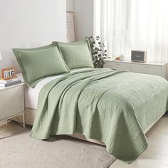 a bed with green bedspread and pillows in a room next to a window