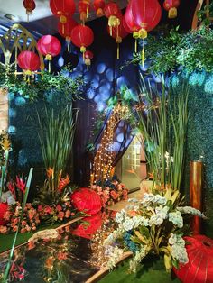 a display with red paper lanterns and flowers in it's centerpieces, surrounded by greenery