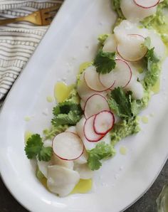 a white plate topped with scallops covered in radishes and cilantro