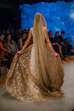 a woman is walking down the runway wearing a gold dress with long veil on her head