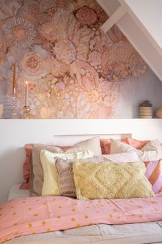 a bed with pink and yellow pillows on top of it next to a wall mural