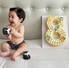 a baby sitting on a bed next to a cake with the number six spelled out