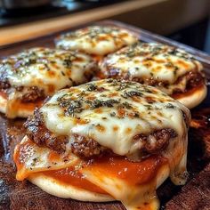 three cheeseburger sandwiches sitting on top of a wooden cutting board in front of an oven