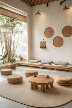 a living room with round wooden tables and pillows on the floor in front of large windows