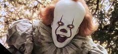 a creepy clown with red hair and white makeup is standing in front of some trees