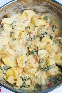 a pot filled with pasta and spinach on top of a white countertop next to utensils