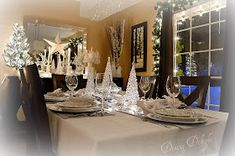 a dining room table set for christmas with white plates and silverware on the place setting