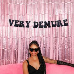 a woman sitting on top of a pink couch in front of a very demure sign