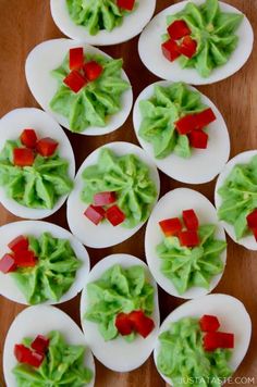 deviled eggs decorated with red peppers and lettuce on white plates sitting on a wooden table