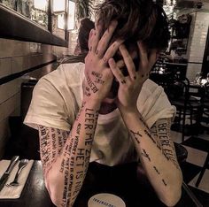 a man sitting at a table with two tattoos on his arms and hands behind his head