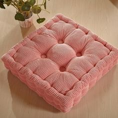 a pink cushion sitting on top of a wooden table next to a potted plant