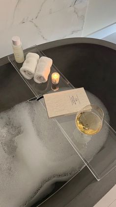 a bathtub with soap, candles and towels on it next to a glass of wine