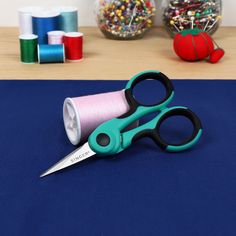 a pair of scissors sitting on top of a blue table next to spools of thread