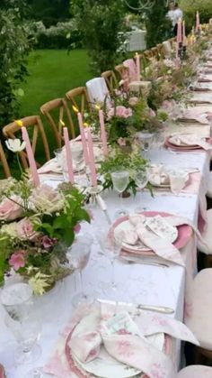 a long table is set with pink and white plates, napkins, candles and flowers