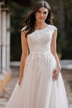 a woman in a white wedding dress standing on a stone walkway with her hand on her hip