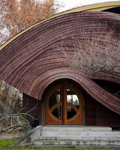 an unusual building with a wooden door and arched window in the middle of grassy area