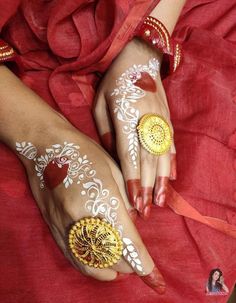 two hands with hendi designs on them and one hand is painted gold, the other has red