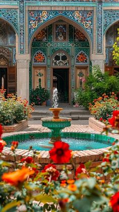 a fountain surrounded by red flowers in front of a building