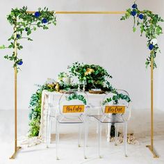 a white table topped with blue flowers and greenery next to a gold metal frame