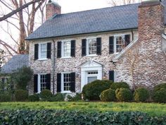 a large brick house with black shutters and white trim on the windows, surrounded by hedges